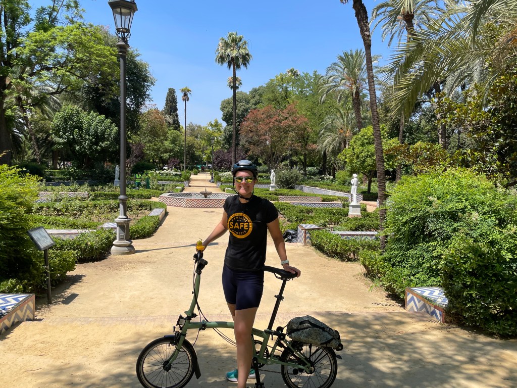 Woman standing next to folding bike in a lush park with a fountain in the background