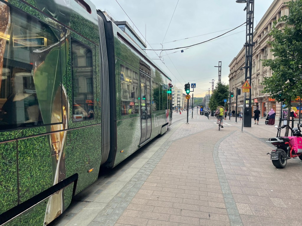A tram goes down a street as a person riding a bike rolls down the dedicated bicycle path. 