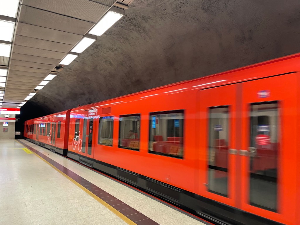 A red subway car is moving, it has a bike symbol painted on one of the doors. 