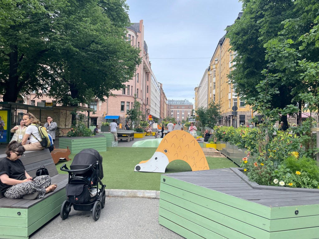 A street is closed to cars - instead, it is open to people playing, lounging, and socializing.